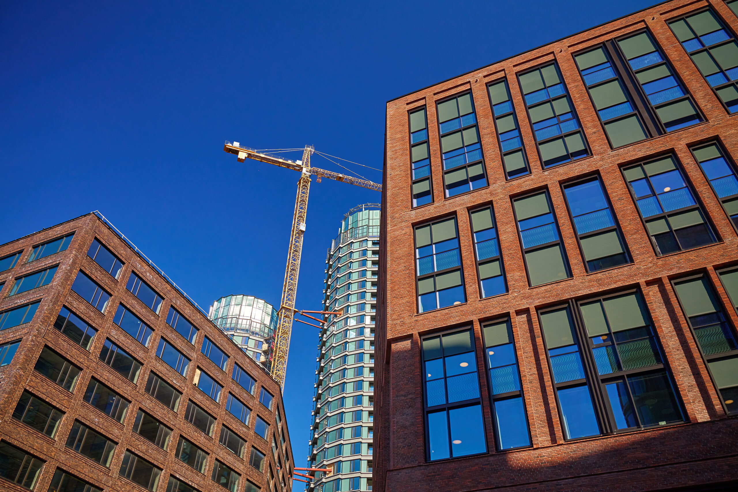 Modern brick buildings and construction crane against vibrant blue sky. Construction of new housing, development of real estate market